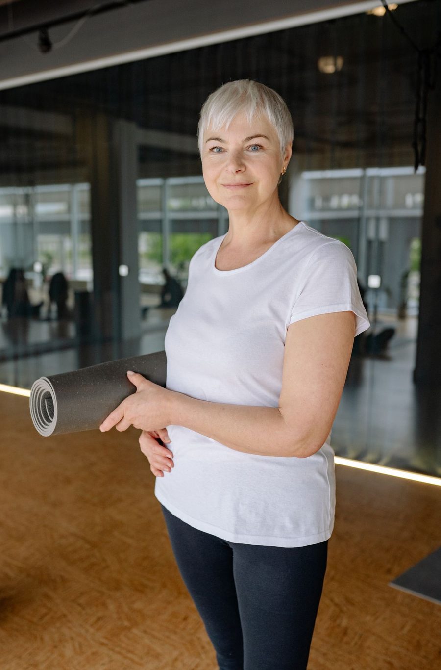 Portrait of Tetiana Nezhuryna, a smiling yoga instructor in a white t-shirt standing in a yoga studio